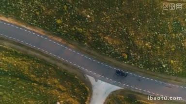 从空中拍摄的驾驶黑色汽车在海边<strong>悬崖</strong>附近的乡村公路的田野上